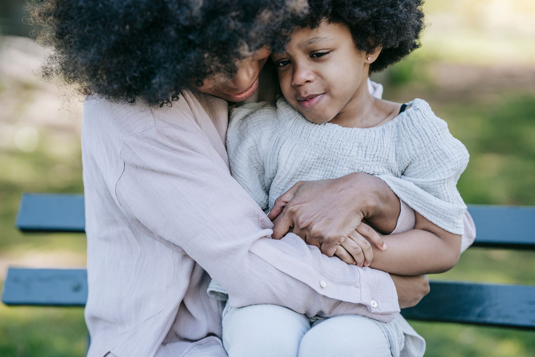 A mother holding and comforting her upset child on a park bench