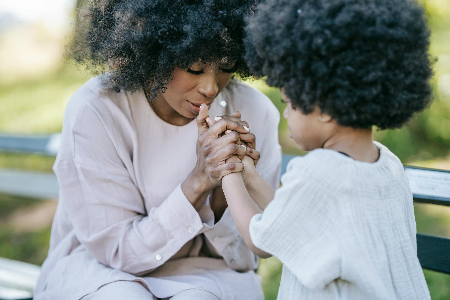 A mother gently holding her young child's hands while they talk